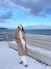 a lady wears a beige wool coat with white turtleneck top and white pants